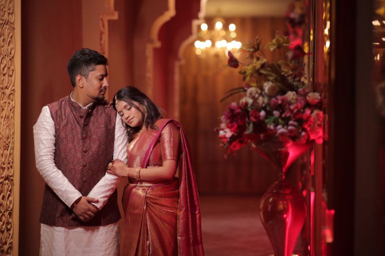 Couple in traditional wedding outfits posing beside floral decoration at a wedding in Noida