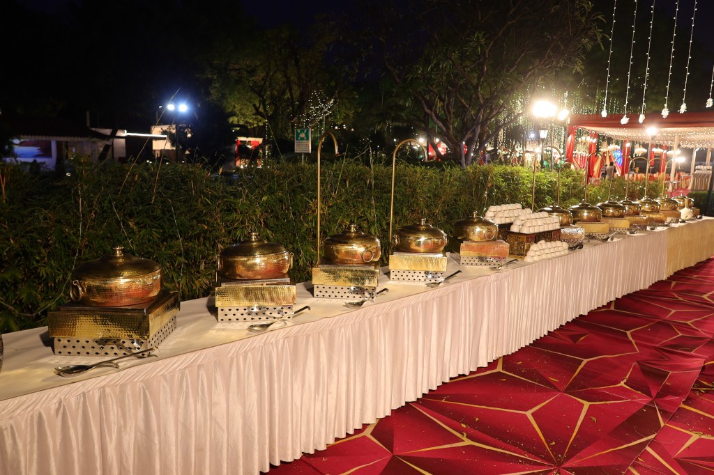 Long outdoor buffet counter with brass chafing dishes at a farmhouse wedding